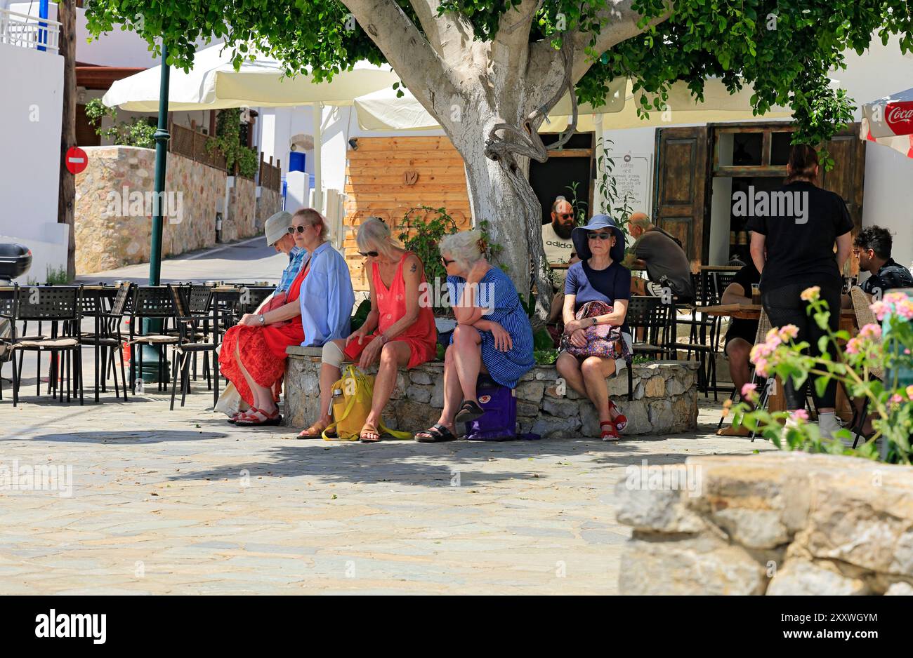Turisti che si rifugiano dal sole mentre aspettano l'autobus, Piazza Livadia, Isola di Tilos, Dodecaneso, Grecia. Foto Stock
