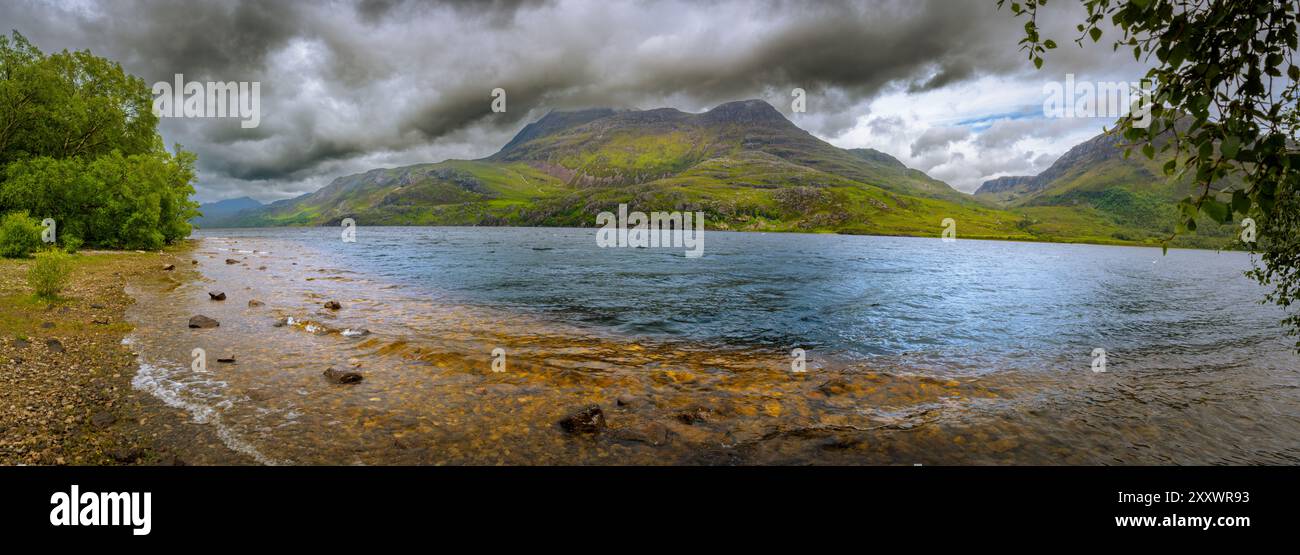 Le scintillanti acque di Loch Maree riflettono le torreggianti montagne verdi, mentre le nuvole scure si innalzano sopra, creando un'atmosfera accattivante. Foto Stock