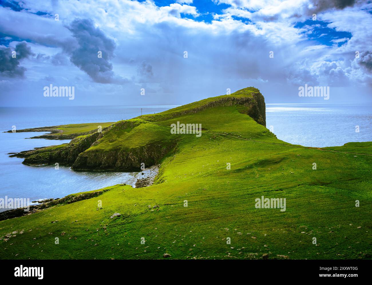 Una vista mozzafiato da Neist Point mostra torreggianti scogliere sullo sfondo di nuvole scure, con acque calme che riflettono la luce che svanisce. Il landsc Foto Stock