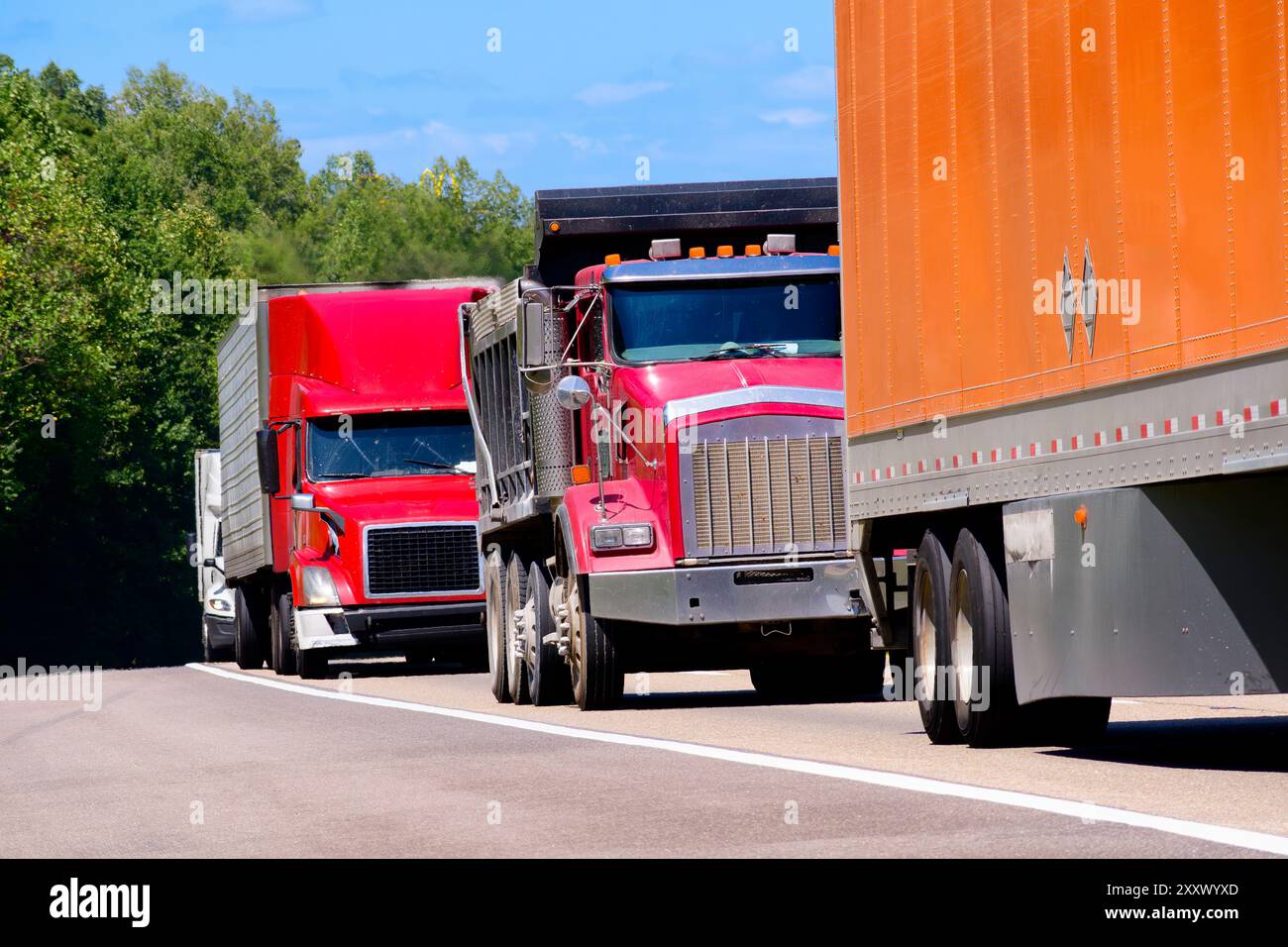 Immagine orizzontale di un convoglio di camion pesanti impilati sull'autostrada interstatale. Le onde di calore che si sollevano dall'asfalto caldo creano un effetto sfocato sul bac Foto Stock