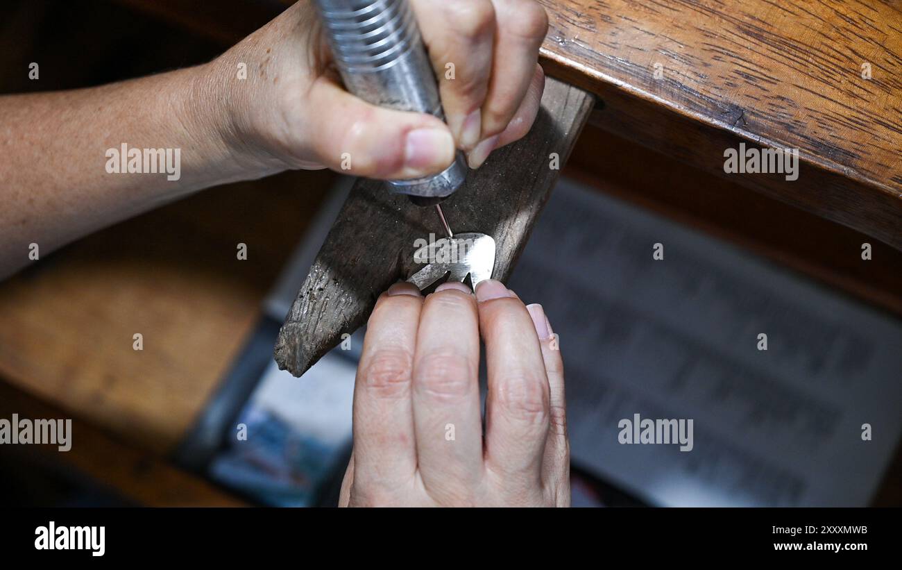 Goldsmith incide su un tavolo di legno un piatto d'argento con un attrezzo elettrico Foto Stock