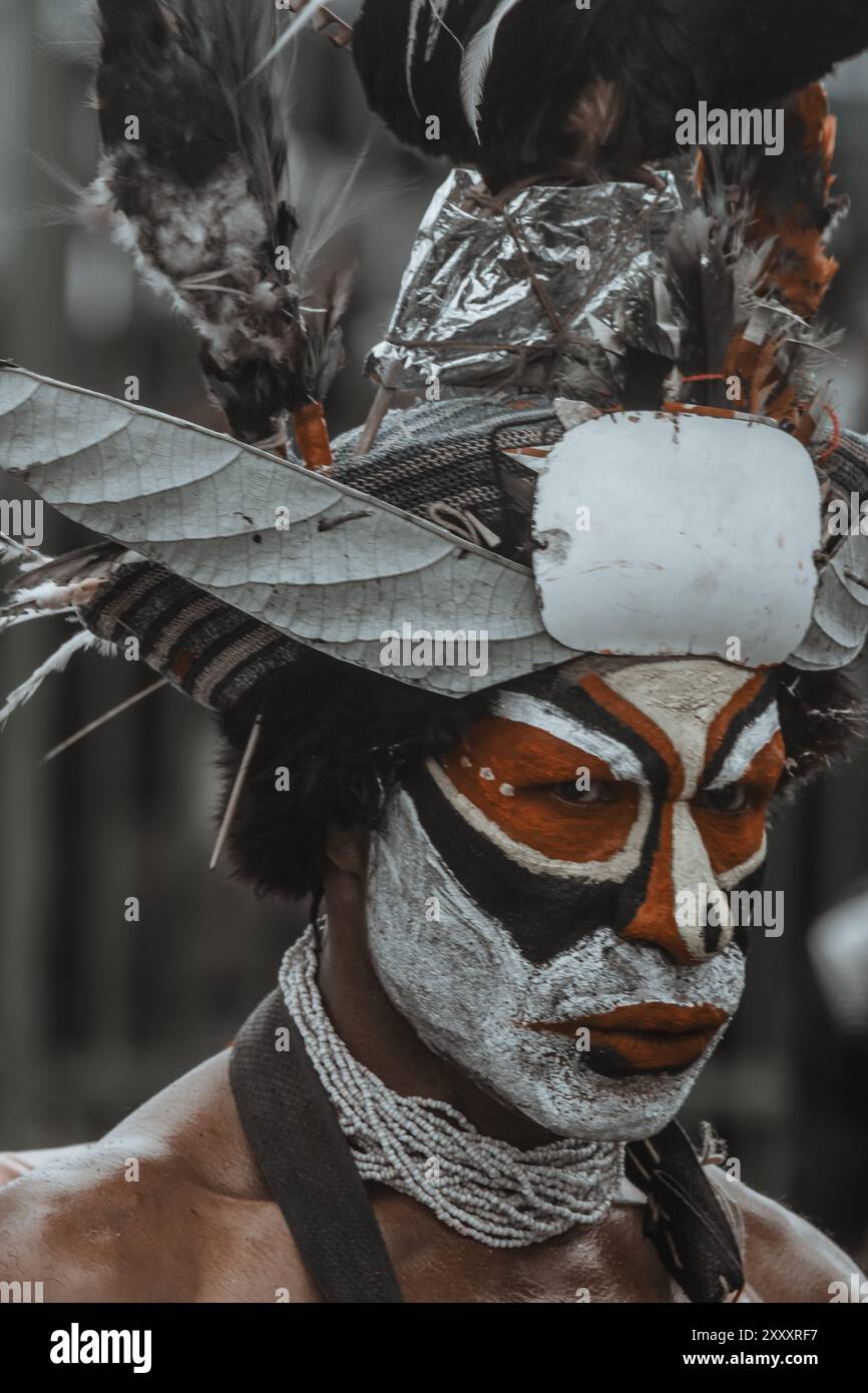 Guerriero delle Highlands della Papua nuova Guinea, con il volto decorato con colori audaci, un grande copricapo piumato, lancia in mano e calci ferocemente. Foto Stock