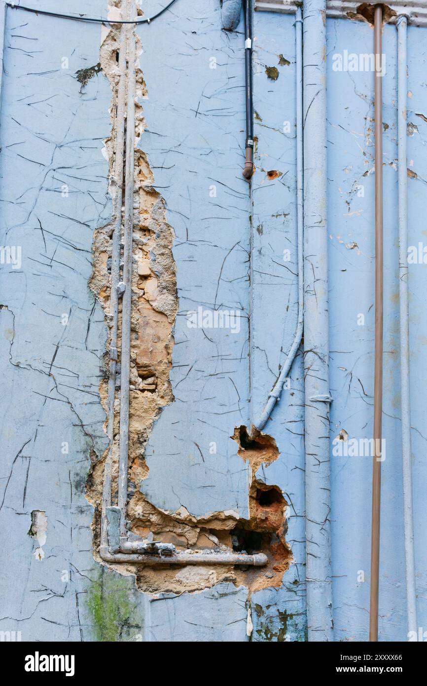 Vecchi tubi esposti su pareti rotte con vernice blu sbucciante Foto Stock