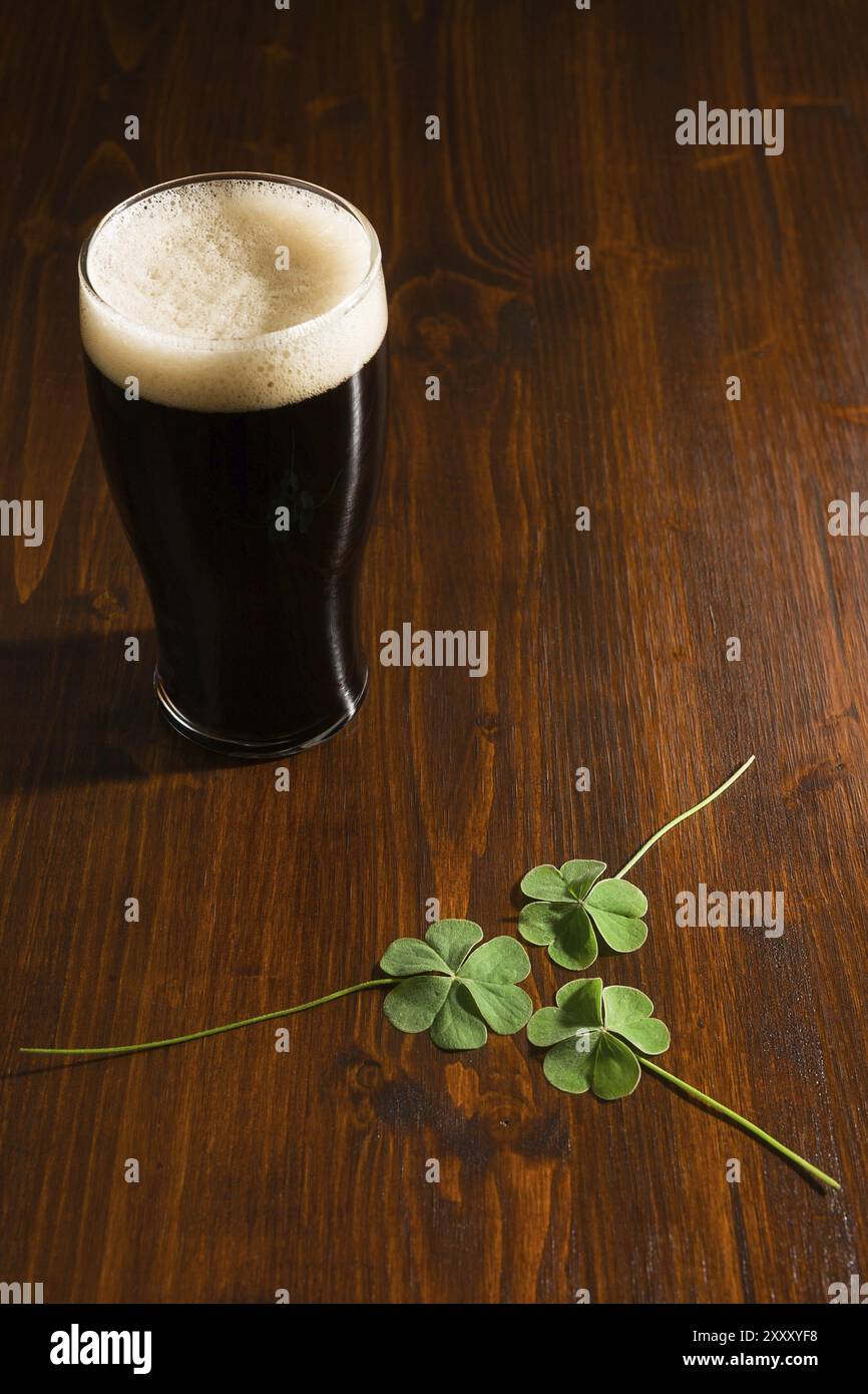 Una pinta di birra nera e tre shamrock su sfondo di legno Foto Stock