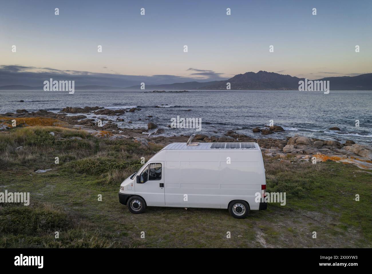 Camper camper con pannelli solari, vista aerea su un paesaggio marino con montagne che vivono la vita in furgone a Galiza, Spagna, Europa Foto Stock