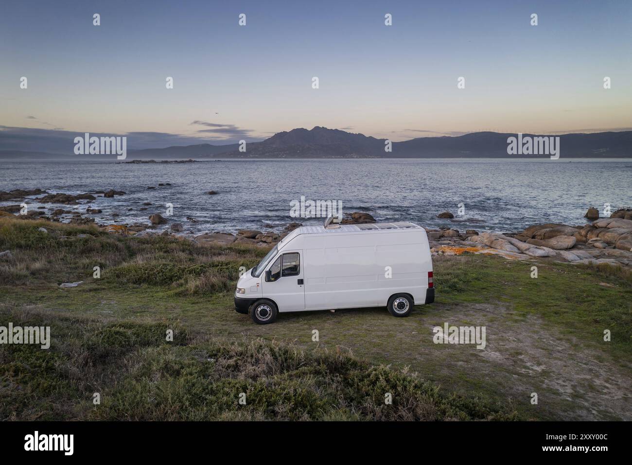 Camper camper con pannelli solari, vista aerea su un paesaggio marino con montagne che vivono la vita in furgone a Galiza, Spagna, Europa Foto Stock