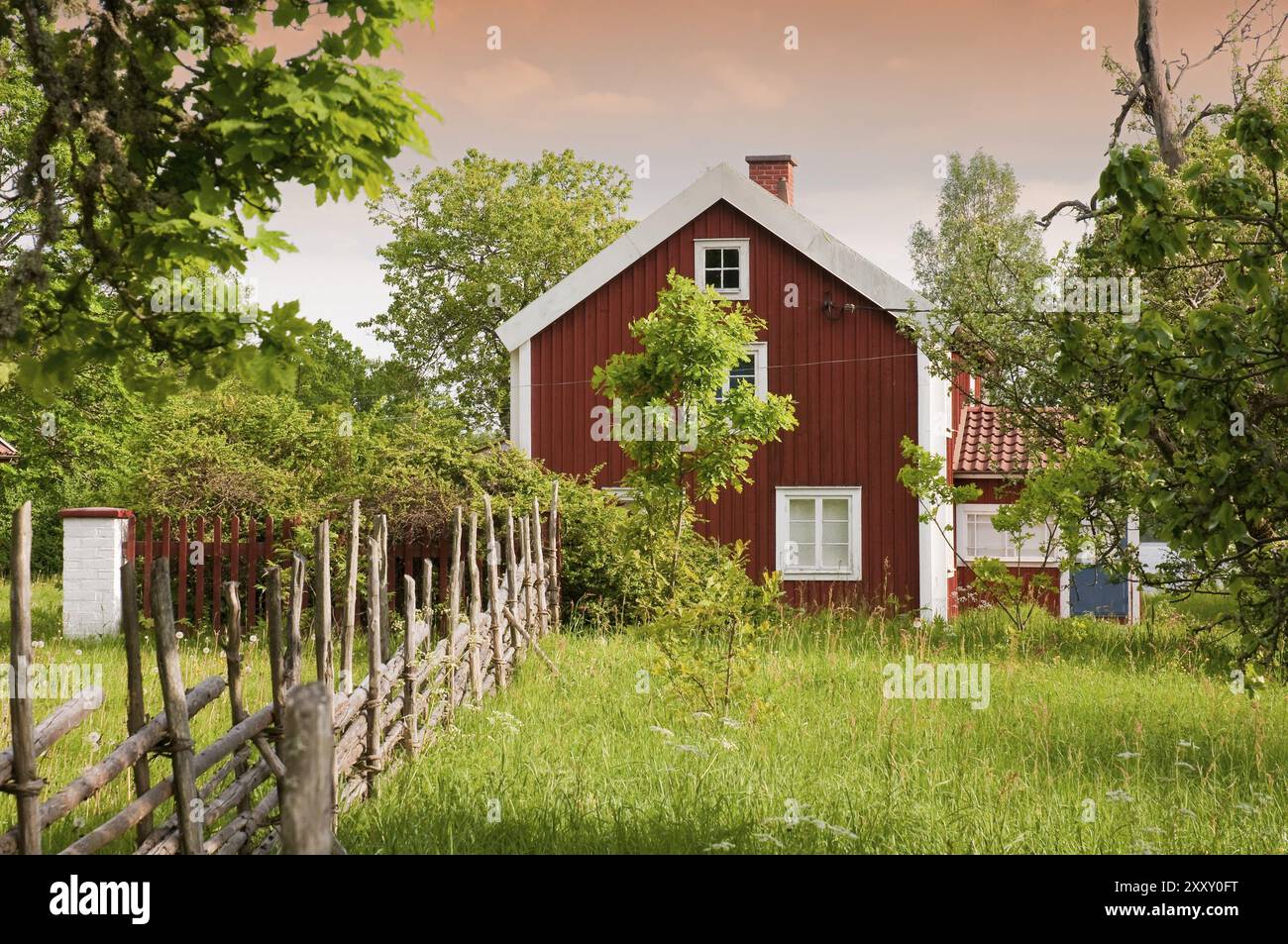 Tipica casa in legno rosso nella Svezia rurale, con recinzione tradizionale, prati e alberi da frutto. Cliche perfette per l'immagine della Svezia nel mondo Foto Stock