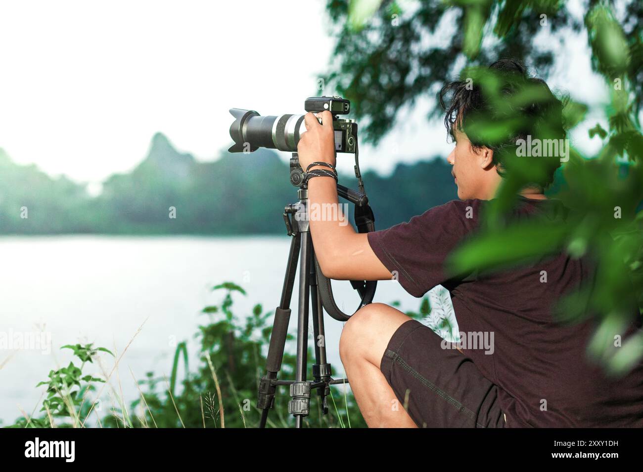 L'uomo cerca di scattare foto vicino al lago con la loro macchina fotografica. Uomo che scatta foto con la fotocamera sul treppiede vicino al lago. Foto dalla vista posteriore Foto Stock