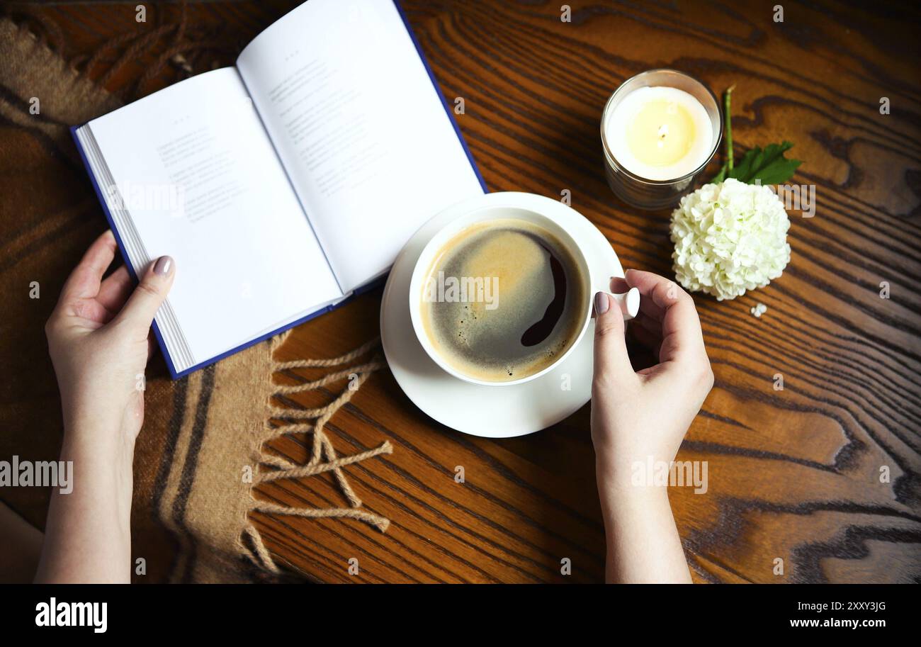 Donna di bere il caffè. Caffè, libro, plaid e candela in casa. Cibo, hygge e concetto di comfort Foto Stock