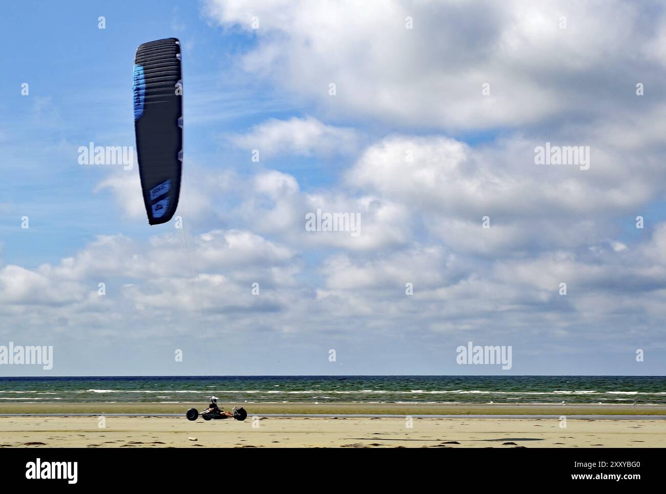 Persona che guida un kite buggy lungo la spiaggia, sotto un cielo azzurro nuvoloso accanto al mare, Sonderhoe, Fanoe, Mare del Nord, Jutland, Danimarca, Europa Foto Stock