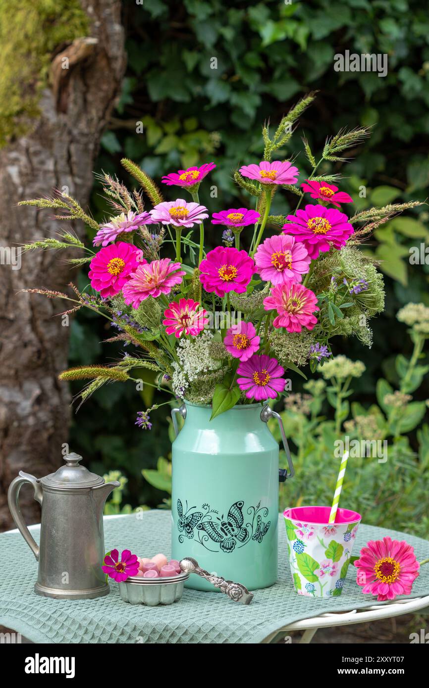 disposizione del tavolo con bouquet di zinnie e erbe rosa, barattolo di caffè, tazza e caramelle Foto Stock