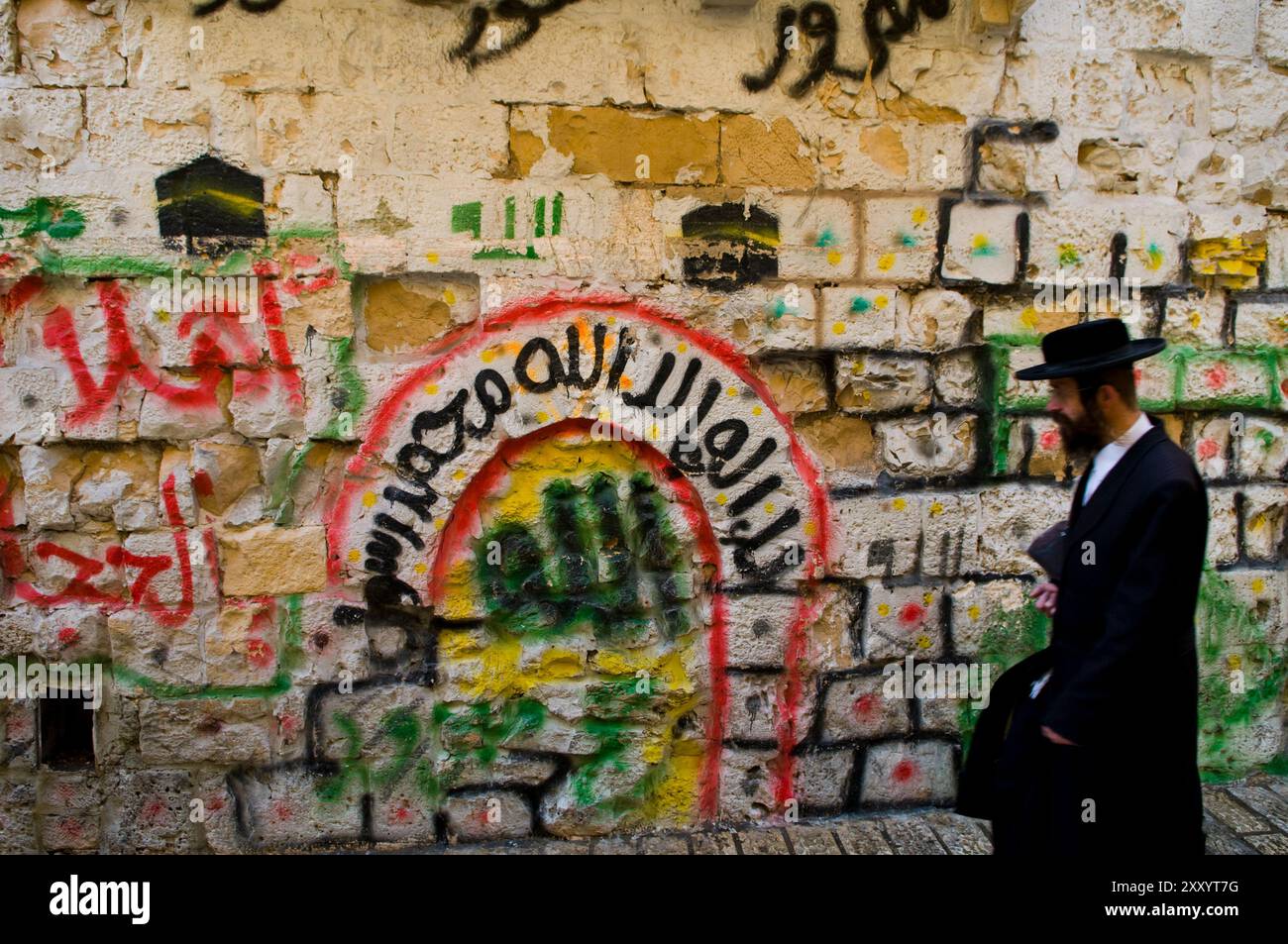 Quartiere musulmano, Gerusalemme. Dicembre 2009.un ebreo ortodosso che cammina accanto ad un muro dipinto con un murale raffigurante l'Hajj, un pellegrinaggio alla Mecca. Foto Stock