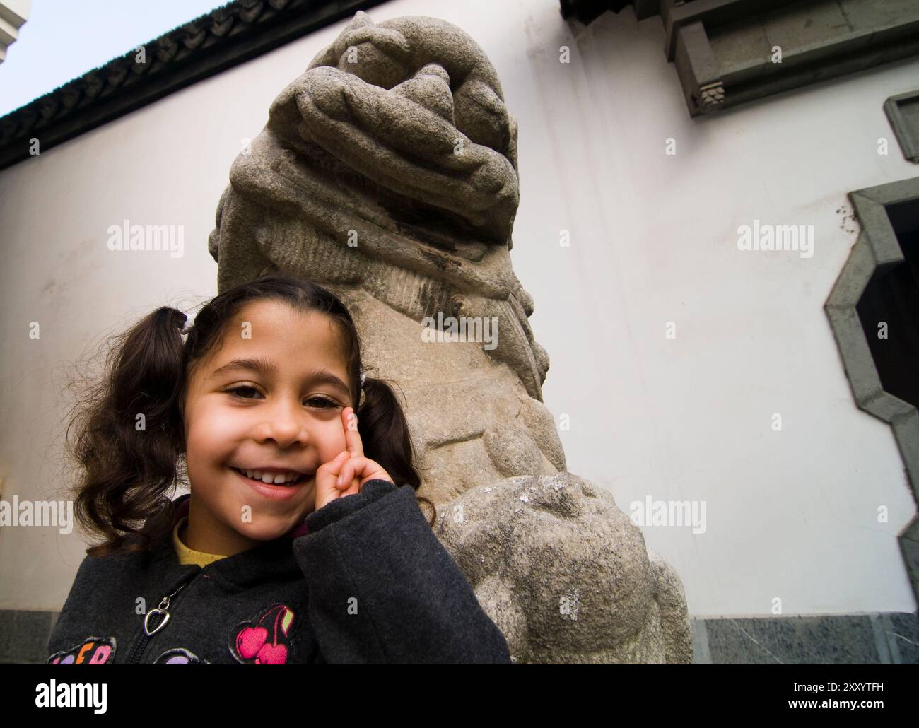 Una ragazza carina che posa sotto un leone custode di un tempio a Nanchino, in Cina. Foto Stock