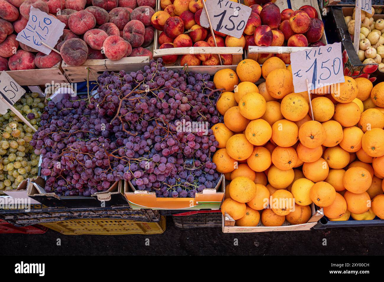 Vivace esposizione di frutta fresca al mercato italiano. Pesche mature, nettarine, uva viola e arance in casse di legno. Etichette dei prezzi in euro sh Foto Stock