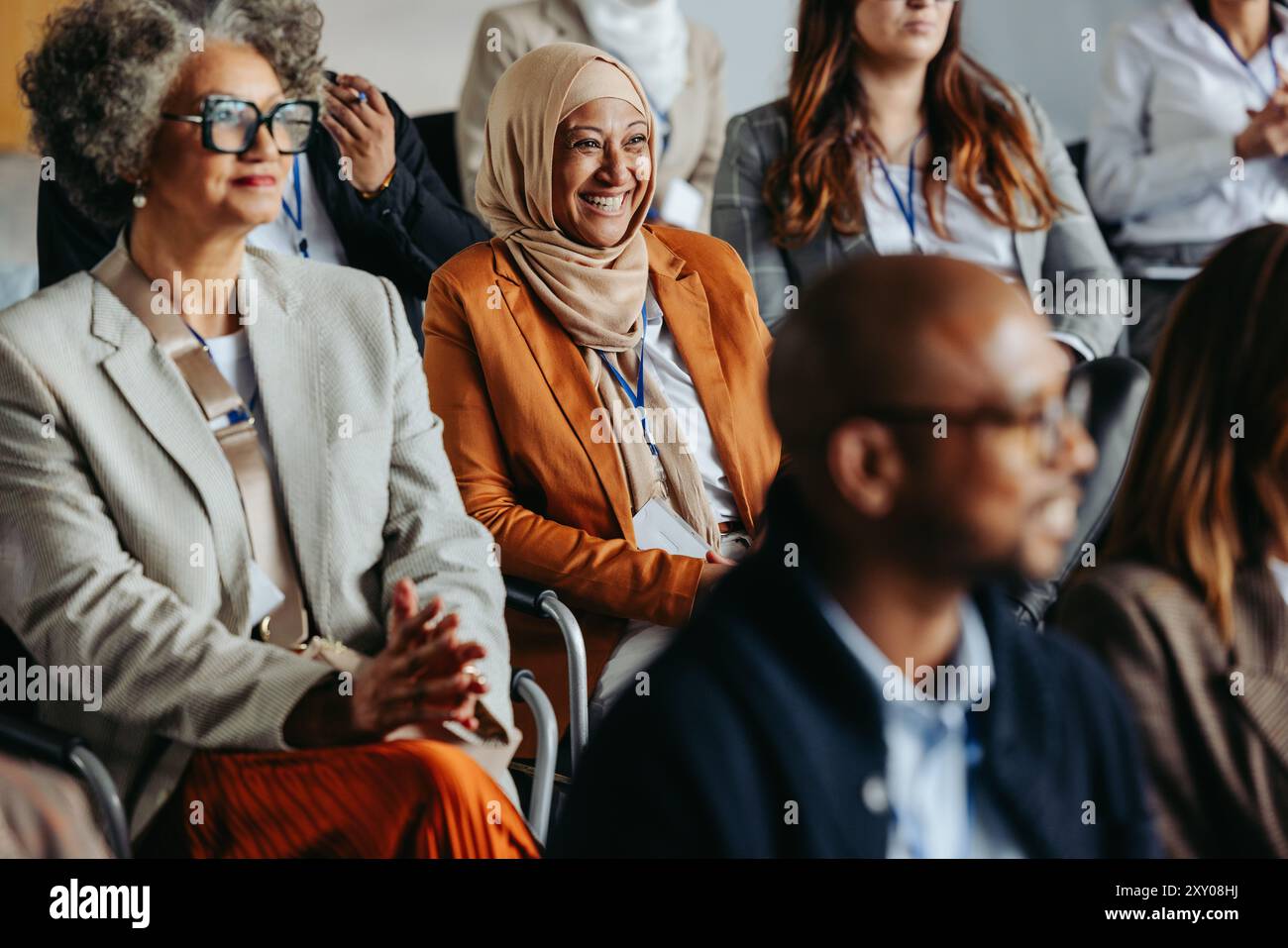 Un gruppo eterogeneo di professionisti, tra cui una donna musulmana sorridente, che partecipa a una conferenza d'affari e ascolta una presentazione. Foto Stock