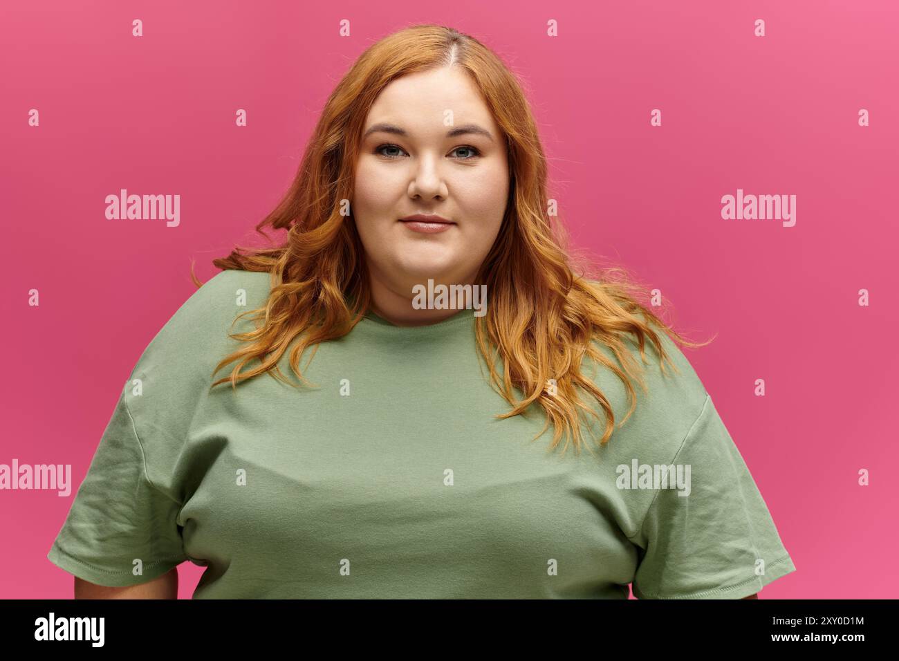 Una donna con lunghi capelli rossi sorride con fiducia mentre indossa una camicia verde. Foto Stock