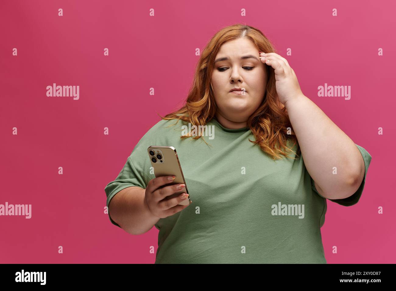 Donna con camicia verde con telefono su sfondo rosa ha un aspetto premuroso Foto Stock