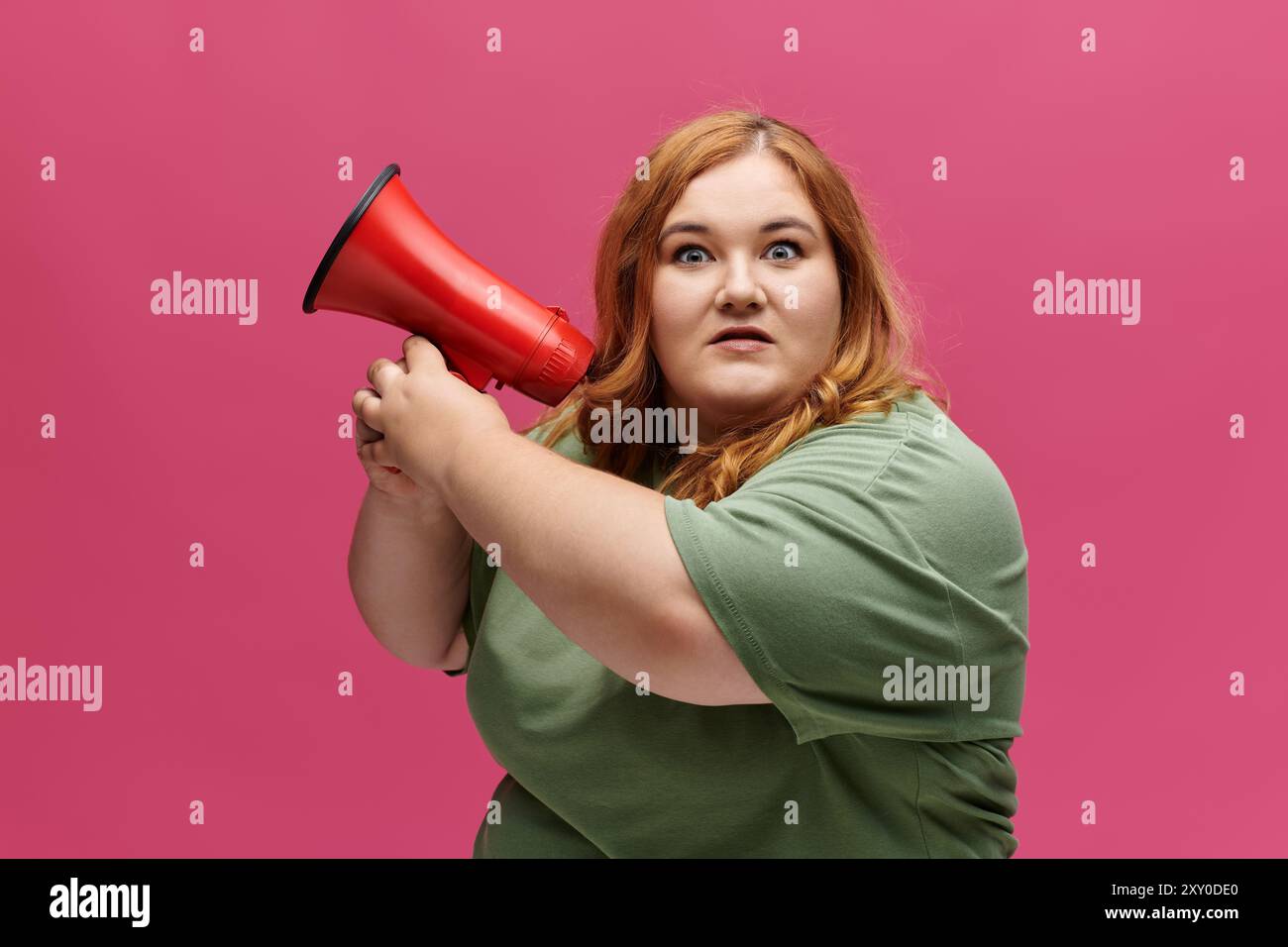 Una donna di grandi dimensioni con capelli rossastri fissa intensamente mentre urla attraverso un megafono rosso. Foto Stock