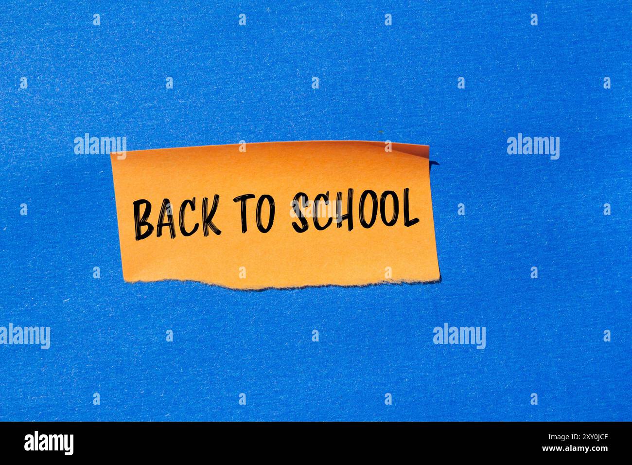Messaggio di ritorno a scuola scritto su un pezzo di carta arancione strappato con sfondo blu. Simbolo concettuale di ritorno a scuola. Copia spazio. Foto Stock