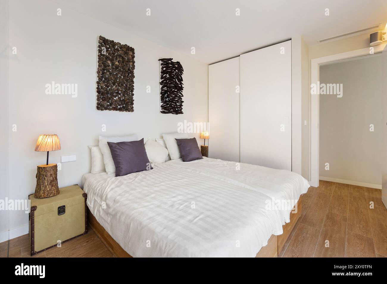 Camera in stile contemporaneo con due letti singoli con biancheria neutra, pareti in alto uniche, pavimento in legno e armadio a muro Foto Stock
