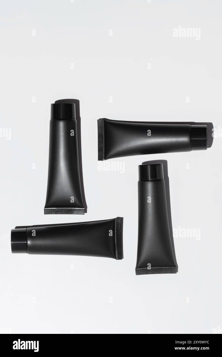Vista dall'alto di un elegante tubo cosmetico nero con tappi, disposti artisticamente su sfondo bianco puro, pronti per il branding. Foto Stock