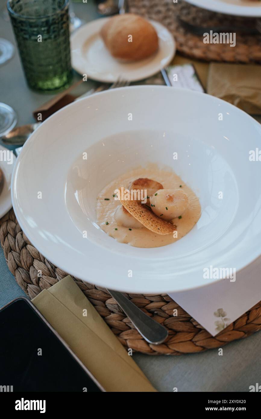 Una fotografia dettagliata di un tavolo da nozze che mostra un piatto sofisticato servito su un piatto bianco incontaminato, completato da un tovagliolo intrecciato ed elegante c Foto Stock