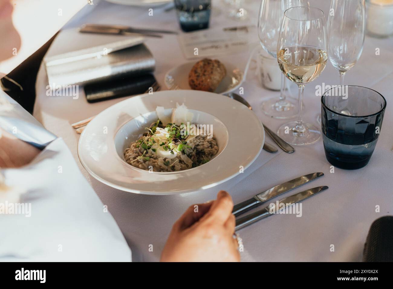Un tavolo da pranzo di nozze splendidamente organizzato con un risotto gourmet, raffinati bicchieri e piatti sofisticati sotto un'illuminazione soffusa Foto Stock