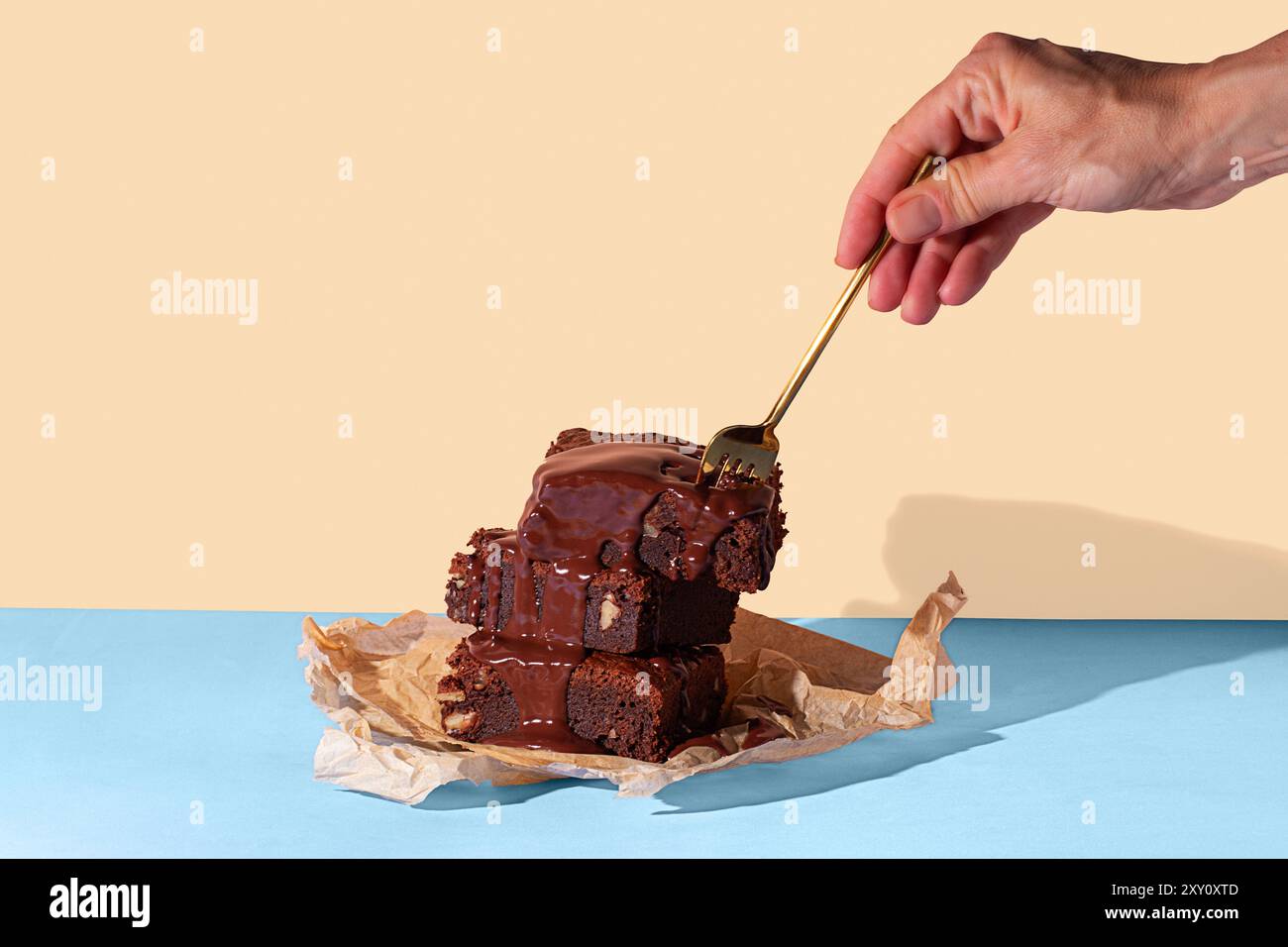 Persona corta e irriconoscibile che versa una ricca salsa di cioccolato su una torre di brownie al cioccolato fatti in casa, serviti su carta pergamena con un dorso bicolore Foto Stock