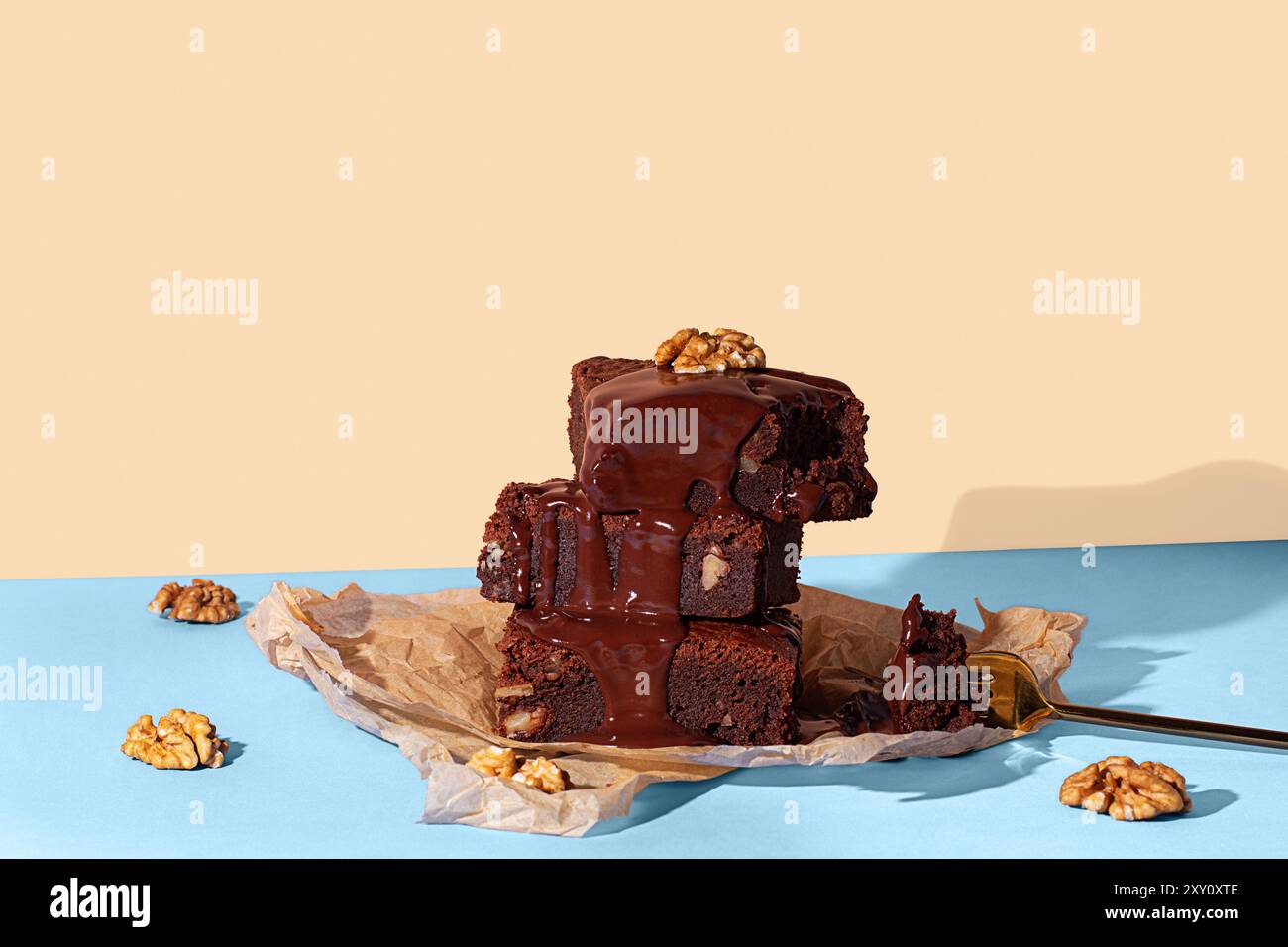 Un'allettante esposizione di brownie al cioccolato fatti in casa impilati e conditi con una ricca e lucida salsa al cioccolato e noci, presentati su un blu a contrasto Foto Stock