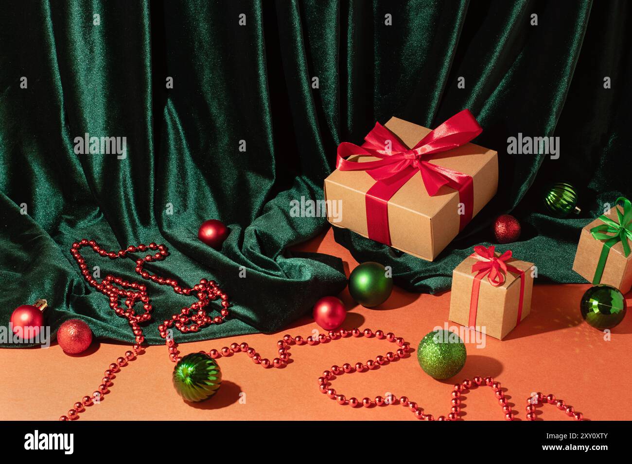 Scatole regalo natalizie con nastri rossi e verdi, circondate da ornamenti natalizi e tessuto di velluto verde Foto Stock