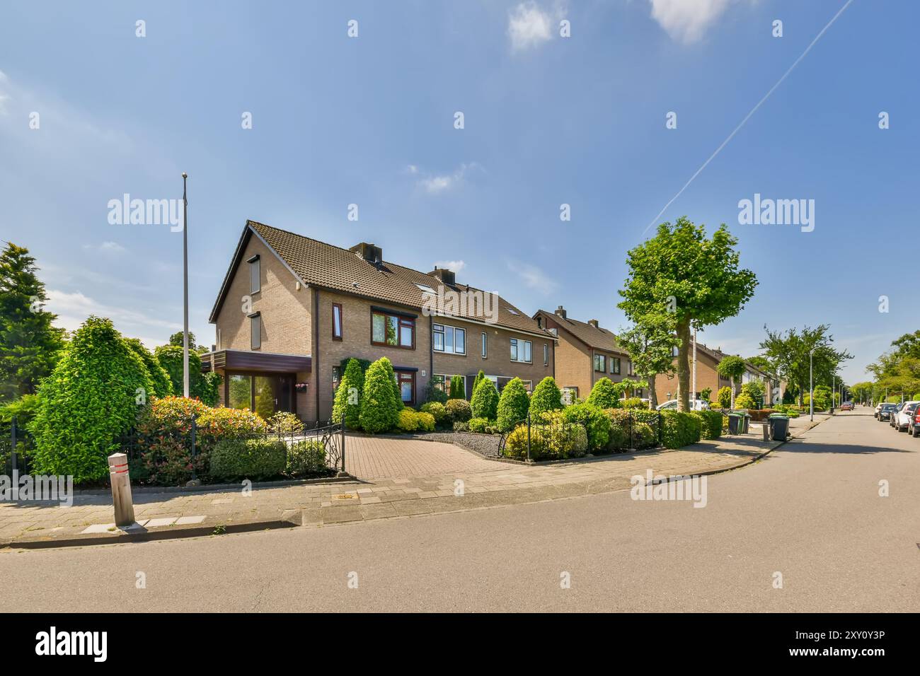 Una tranquilla strada suburbana presenta una fila di case a schiera contemporanee con giardini ben tenuti sotto un cielo blu luminoso. Foto Stock