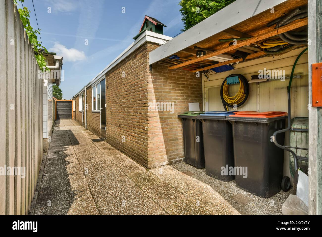 Un vicolo ben tenuto tra edifici in mattoni con spazio per riporre utensili da giardino e bidoni sotto un riparo in legno. Foto Stock