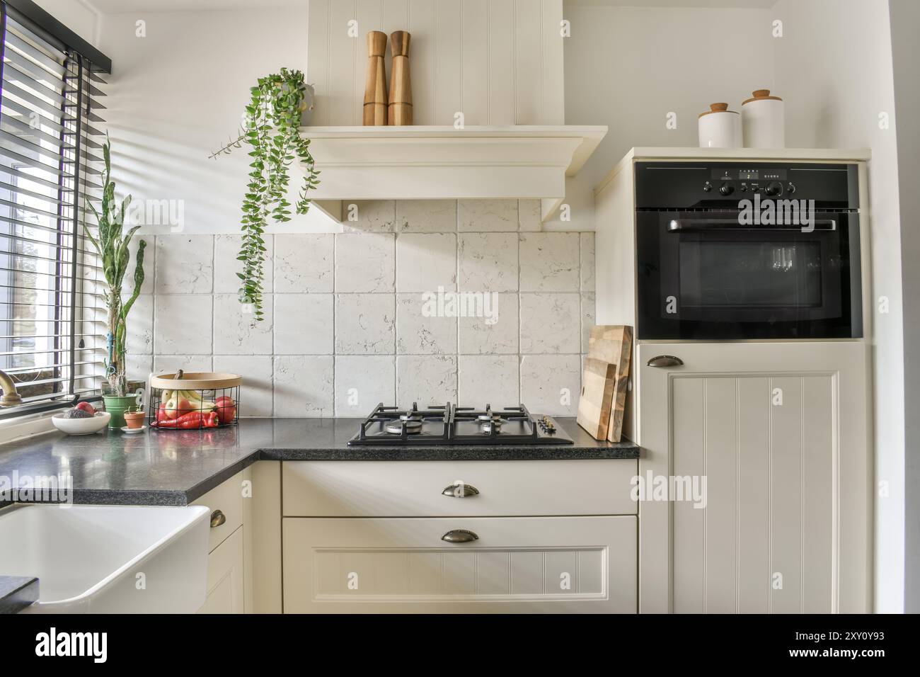 Una cucina moderna, luminosa ed elegante, dotata di lavello in agriturismo, fornelli a gas ed eleganti mobili bianchi con luce naturale che si diffonde attraverso la vittoria Foto Stock