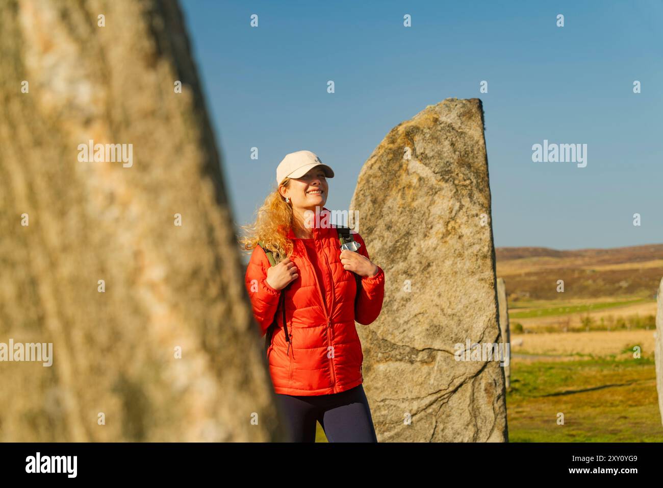 Una giovane donna gode dell'atmosfera tranquilla dei Callanish Stones sull'isola di Lewis, in Scozia, durante le ore d'oro del tramonto, il suo joyfu informale Foto Stock