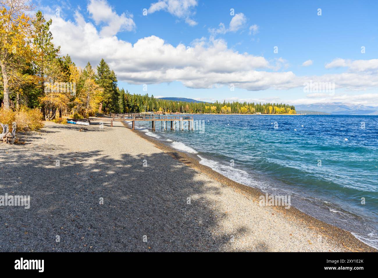 Spiaggia deserta di ciottoli con moli di legno delimitati da boschi su un lago in una giornata d'autunno soleggiata e ventosa. Colori autunnali. Foto Stock