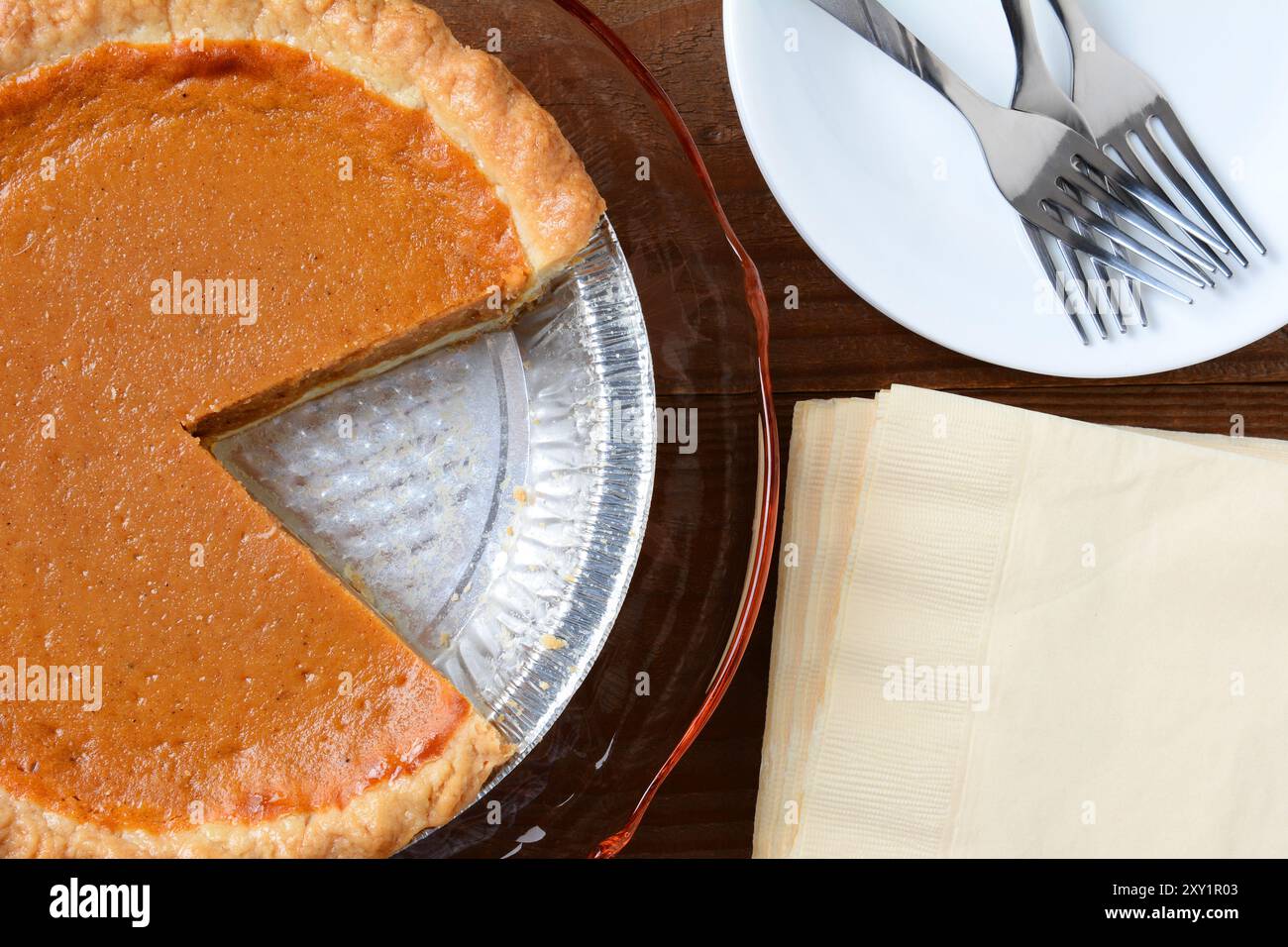 Vista dall'alto di una torta di zucca natalizia con una fetta tagliata. Formato orizzontale con tovaglioli, piastra e forche. Foto Stock