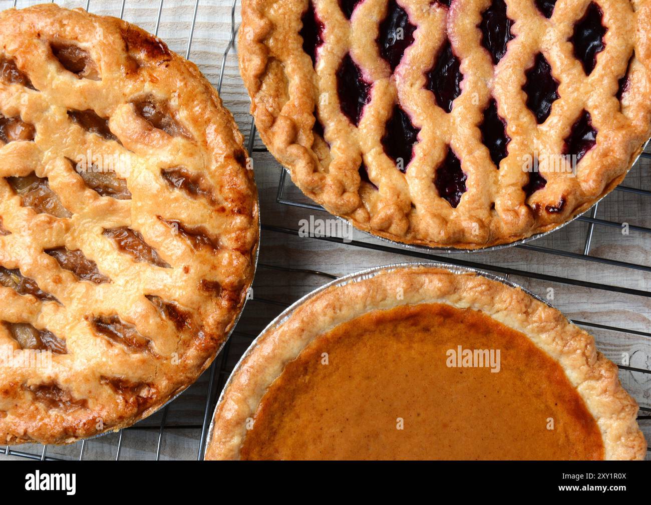 Tre torte su rack refrigeranti. Primo piano ad angolo alto di torte di mele, ciliegie e zucca appena sfornate su un tavolo da cucina in legno rustico. Oriz Foto Stock