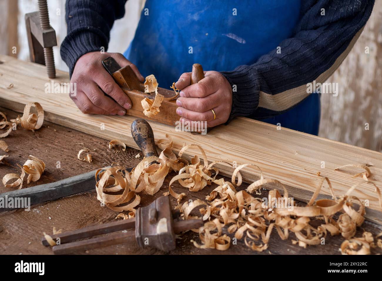 Primo piano di un artigiano che plana a mano una tavola di legno, con trucioli di legno ricci in un laboratorio tradizionale Foto Stock