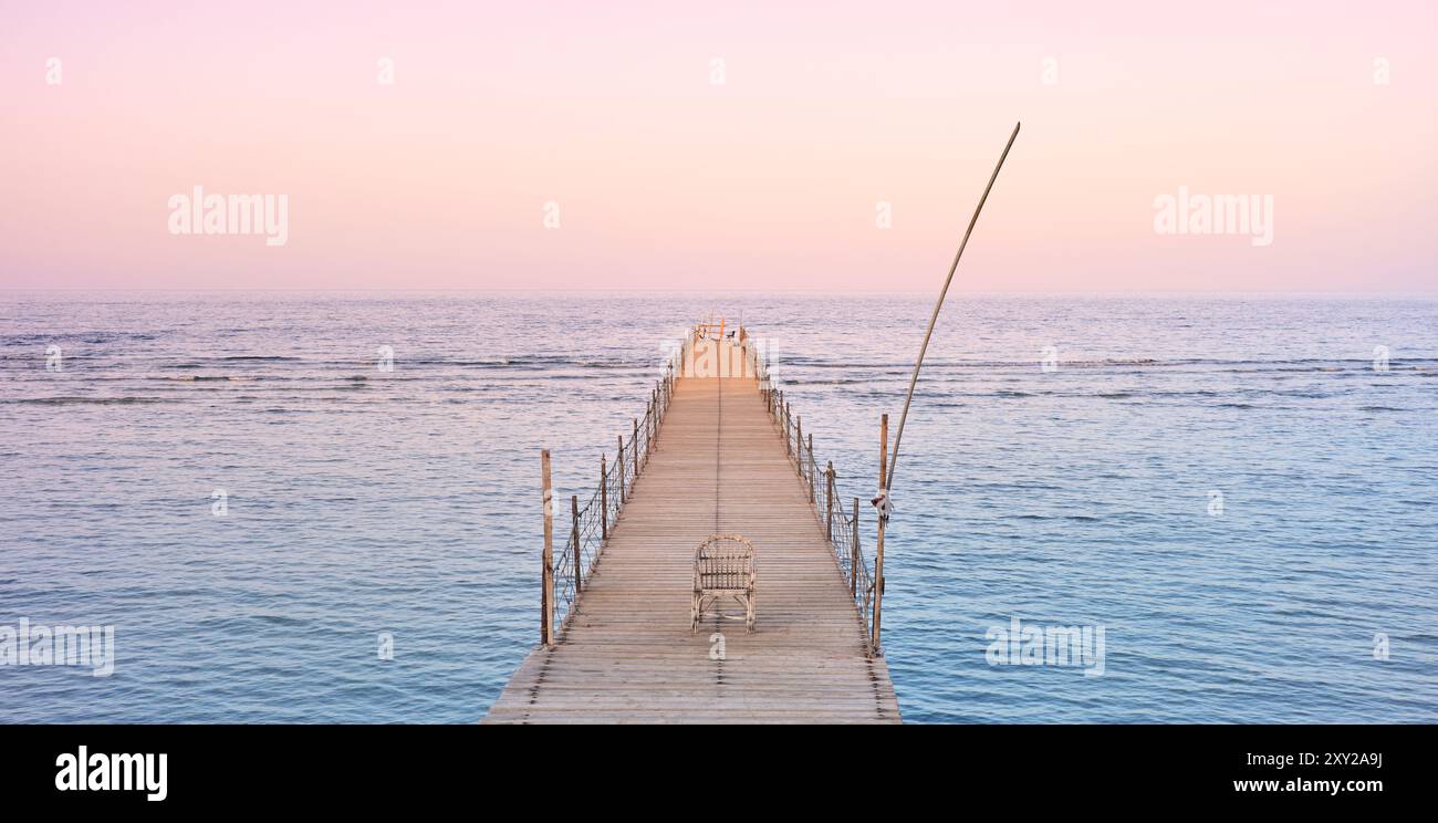 Foto di una sedia vuota su un molo di legno a un tramonto viola. Foto Stock