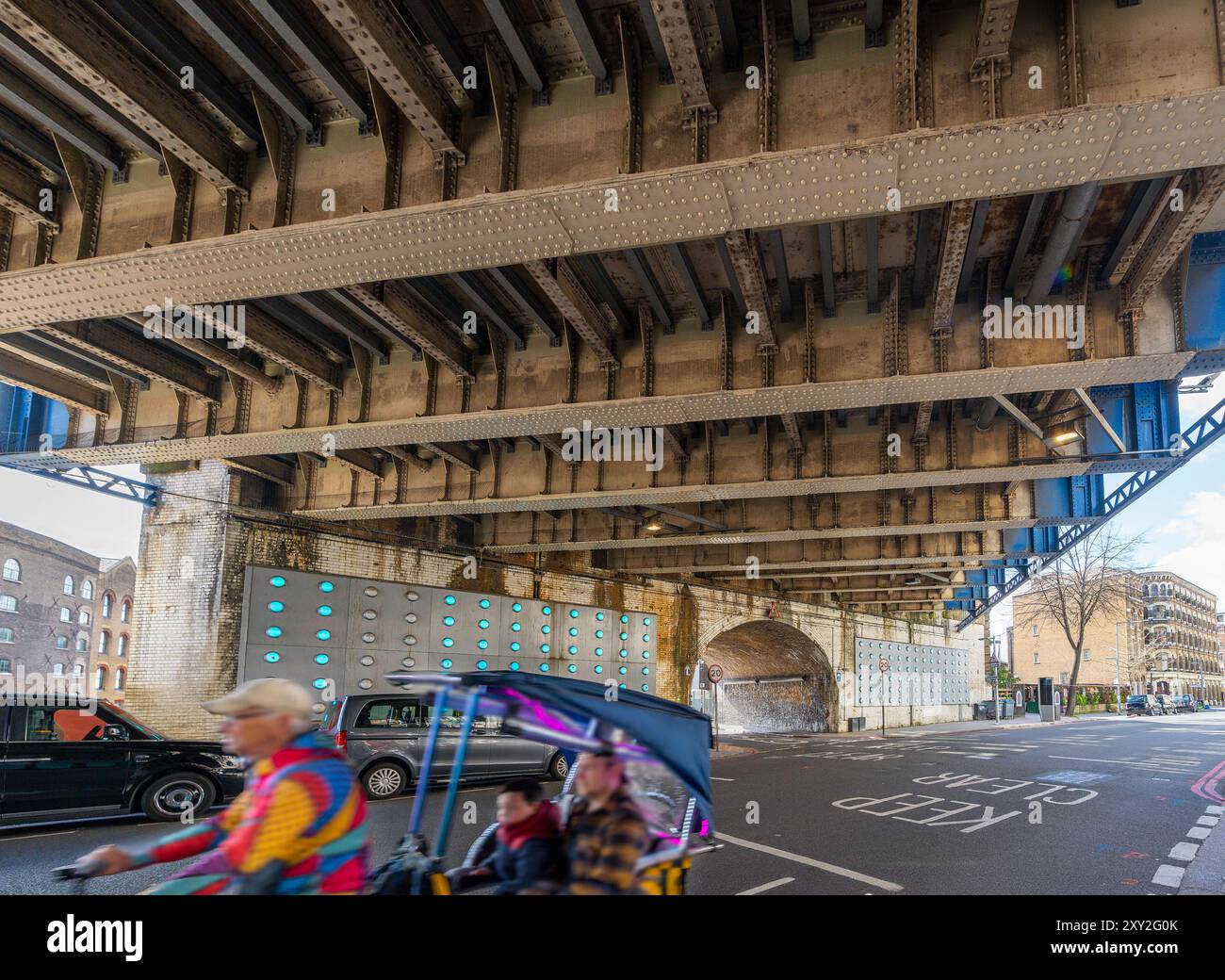 Sotto il ponte ferroviario di Southwark Street con un uomo più anziano che guida un taxi per moto a tre ruote con un padre e un figlio che visitano Londra, EN Foto Stock