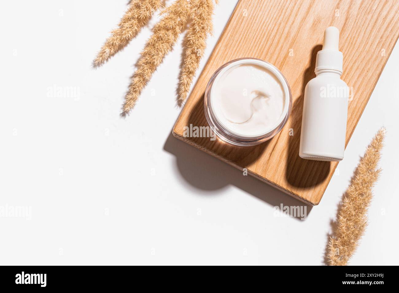 Siero cosmetico e crema di bellezza con canne secche o erba di pampa isolata su sfondo bianco. Trattamento viso anti-invecchiamento naturale della pelle, spazio di copia. Foto Stock