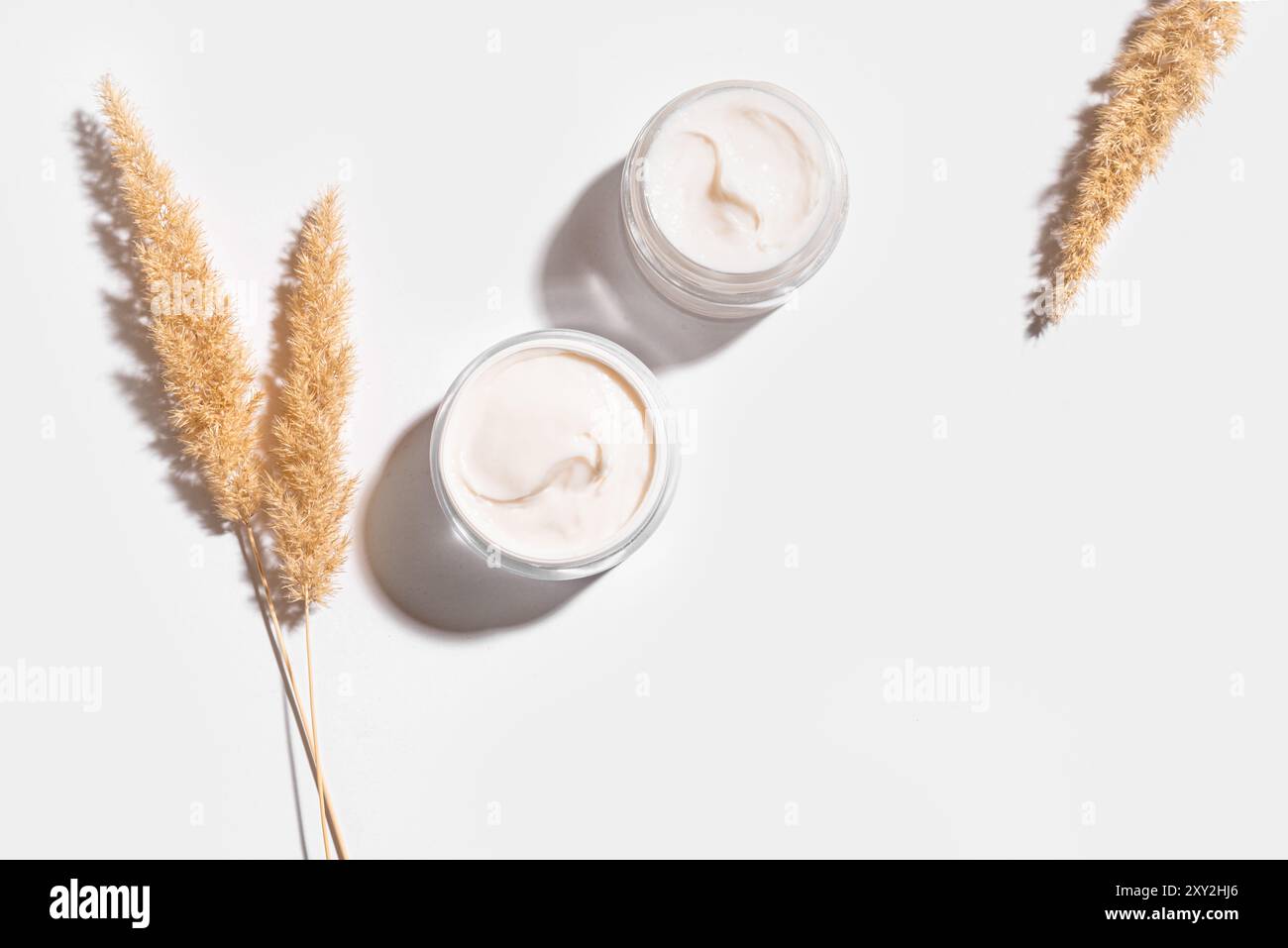 Crema di collagene in vasetti aperti e erba secca isolata su sfondo bianco, vista dall'alto, spazio di copia. Cura naturale della pelle e del corpo anti-invecchiamento professionale Foto Stock