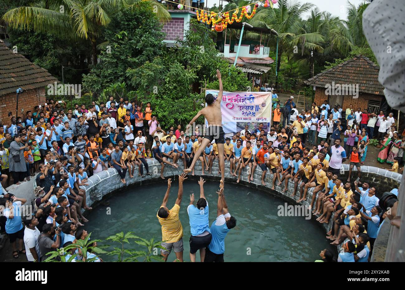 Mumbai, India. 27 agosto 2024. Un devoto salta in aria per rompere una pentola piena di cagliata durante la celebrazione per celebrare il festival indù di Janmashtami in un villaggio di Alibag. Janmashtami è celebrata come la nascita del signore Krishna dai devoti indù cantando canzoni devozionali e digiunando per un giorno fino a mezzanotte. Il giorno successivo Dahi Handi (pentola piena di cagliata) viene celebrato per strada rompendo la pentola piena di cagliata come rievocazione dell'infanzia del signore Krishna, dove spesso rubava cagliata e burro dalla pentola tenuta a un'altezza da sua madre. Credito: SOPA Images Limited/Alamy Live News Foto Stock