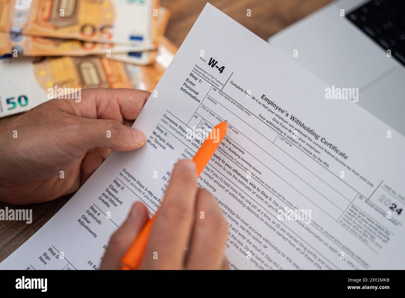 Il libero professionista legge meticolosamente il modulo W-4 al tavolo da pranzo con laptop e bollette in euro Foto Stock