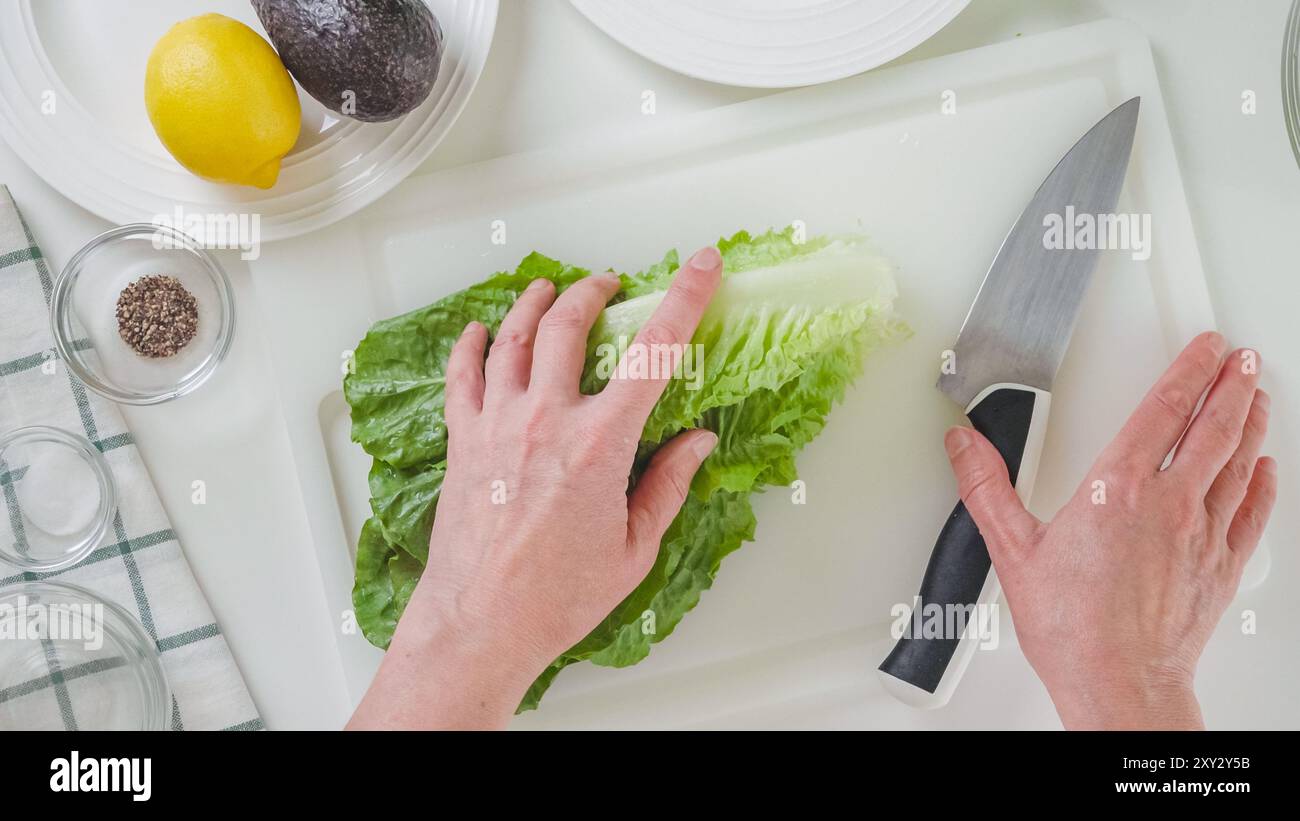 Donna che prepara insalata di sedano con lattuga romagina. Primo piano di foglie di lattuga verde fresca su un tagliere bianco, piatto Foto Stock