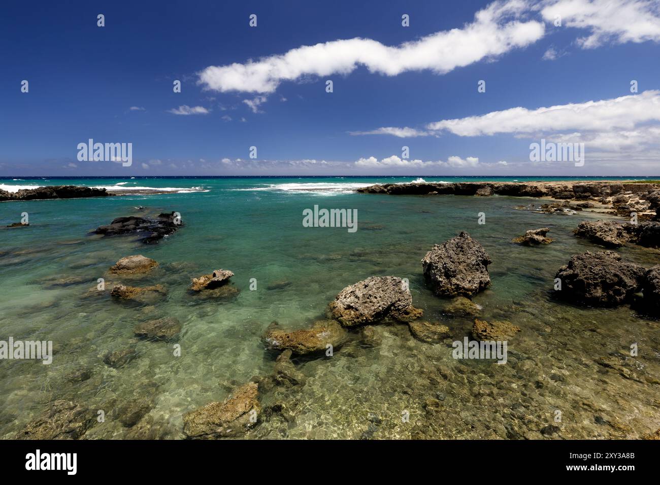 Il litorale roccioso di lava del parco Beach Ponds of Oahu Ka'ena Point Beach Park con acque turchesi, cieli blu e nuvole bianche Foto Stock