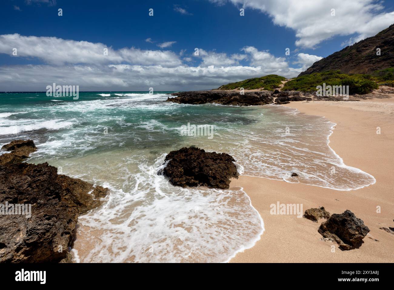 Una giornata di sole con poche nuvole nella remota e incontaminata spiaggia Hawaiana Monk Seal nel Ka'ena Point Beach Park di Oahu, con onde che si estendono sulla spiaggia Foto Stock