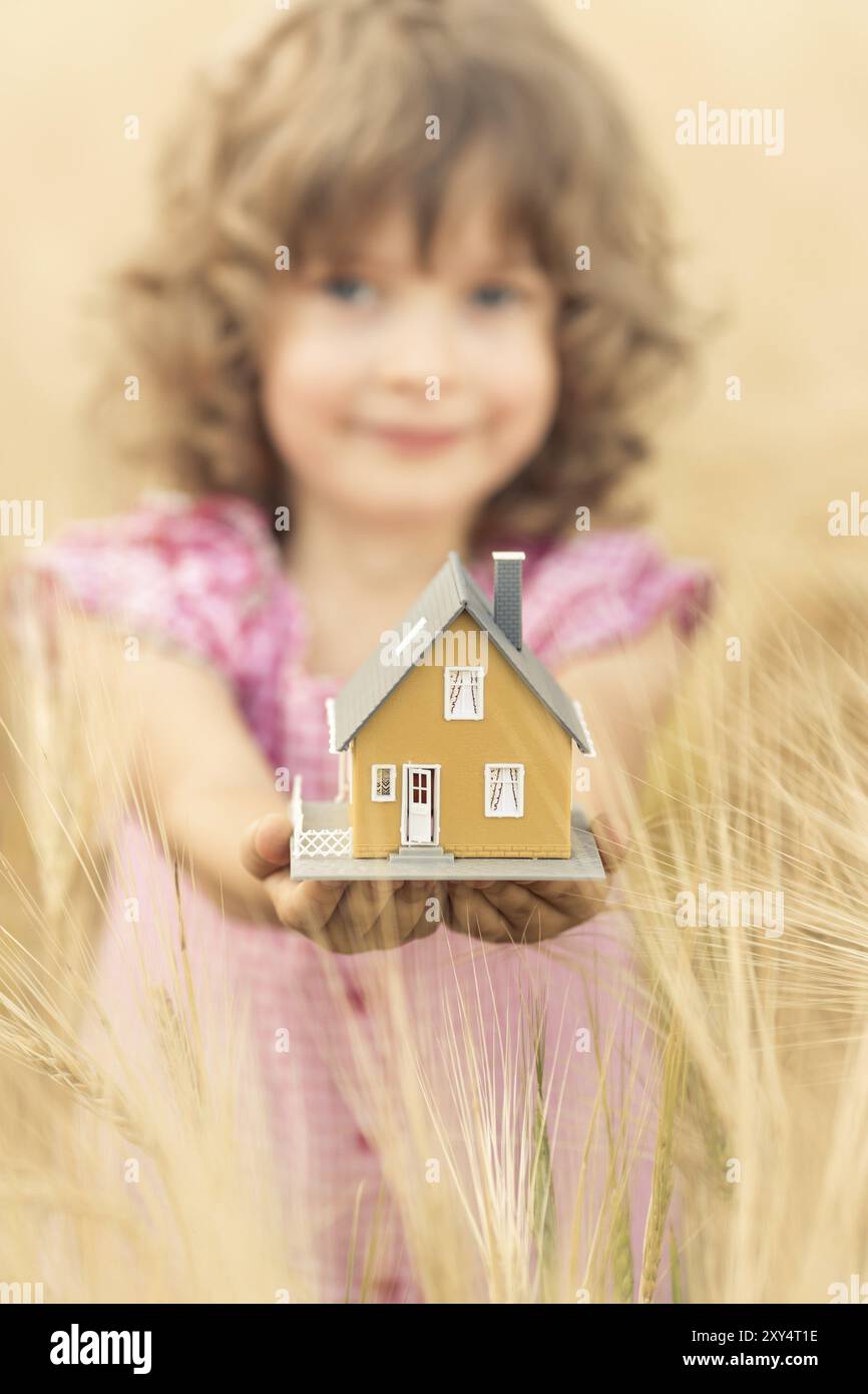 Bambino felice che tiene la casa in mano su sfondo giallo autunnale. Concetto immobiliare Foto Stock