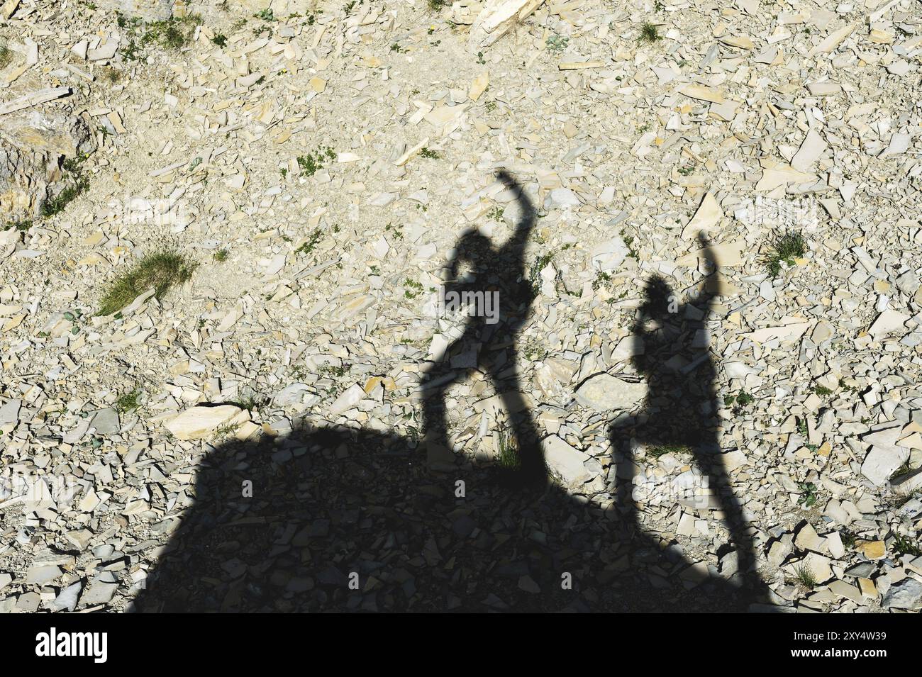 Due ombre di fotografi sulla terra che salgono in salita con mani alzate che urlano di vittoria e successo. Sagome di due persone che camminano in alto Foto Stock