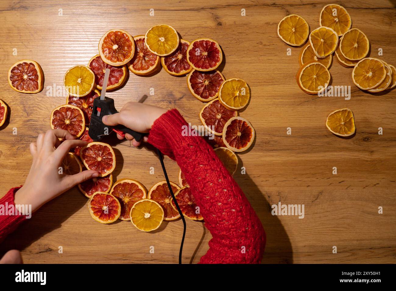 Corona di Natale fatta a mano con fette di pompelmo d'arancia secca. Preparazione per le festività natalizie, maestria nella creazione creativa dell'arredamento. Attività pratiche creazione di un workshop di regali per le festività sostenibili e responsabili. Vista dall'alto, disposizione piatta Foto Stock